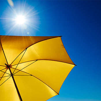 gelber Sonnenschirm mit blauem Himmel und heller Sonne im Hintergrund