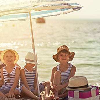 Mutter mit Kindern am Strand unter einem Sonnenschirm. Sie genießen die Zeit am Strand