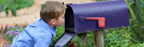 Kleiner Junge schaut in einen blauen Briefkasten im US-Style