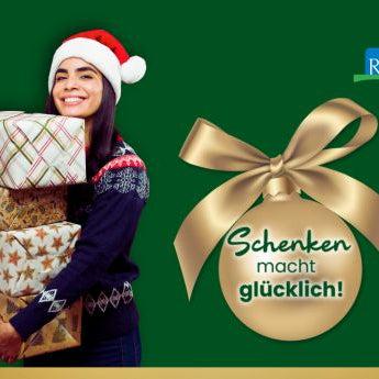 Junge Frau mit Weihnachtsmütze und vier Geschenken im Arm lächelt freundlich – unser Motto "Schenken macht glücklich!