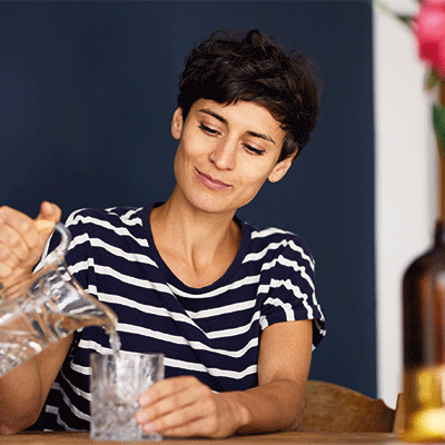 Frau schenkt sich ein Glas Wasser aus einem Krug ein