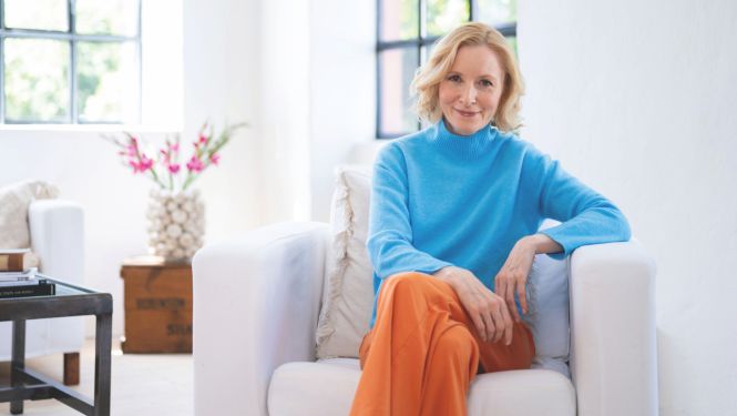 Anne Fleck in einer hellen Wohnung auf einem weißen Sessel sitzend