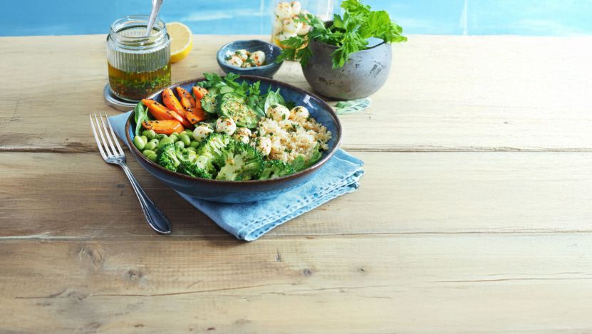 Grüne Salat-Bowl in einem blauen Teller auf Holztisch mit Zutaten angerichtet