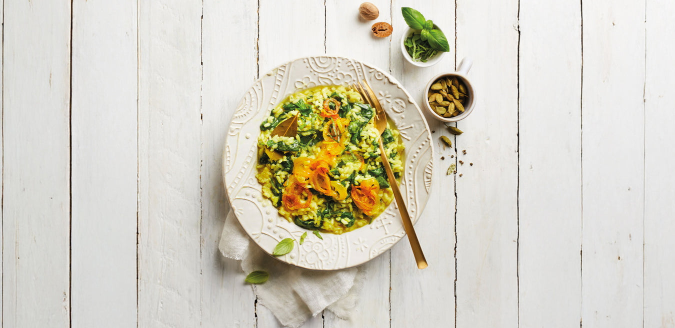 Basilikum-Spinat-Risotto mit Kurkuma-Zwiebeln auf Teller auf weißer Holzplatte