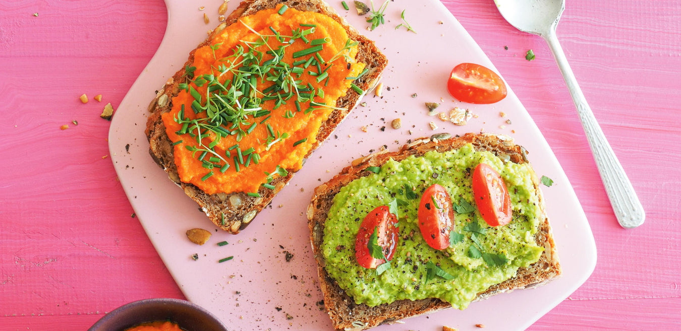 Erbsen-Guacamole auf einem Brot angerichtet mit Brettchen auf pinkem Tisch