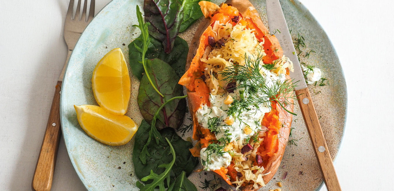 Sükartoffel-Kumpir mit mediterranem Sauerkrautsalat und Quarkdip auf Teller mit zwei Spalten Zitrone, etwas Blattsalat und Messer und Gabel angerichtet