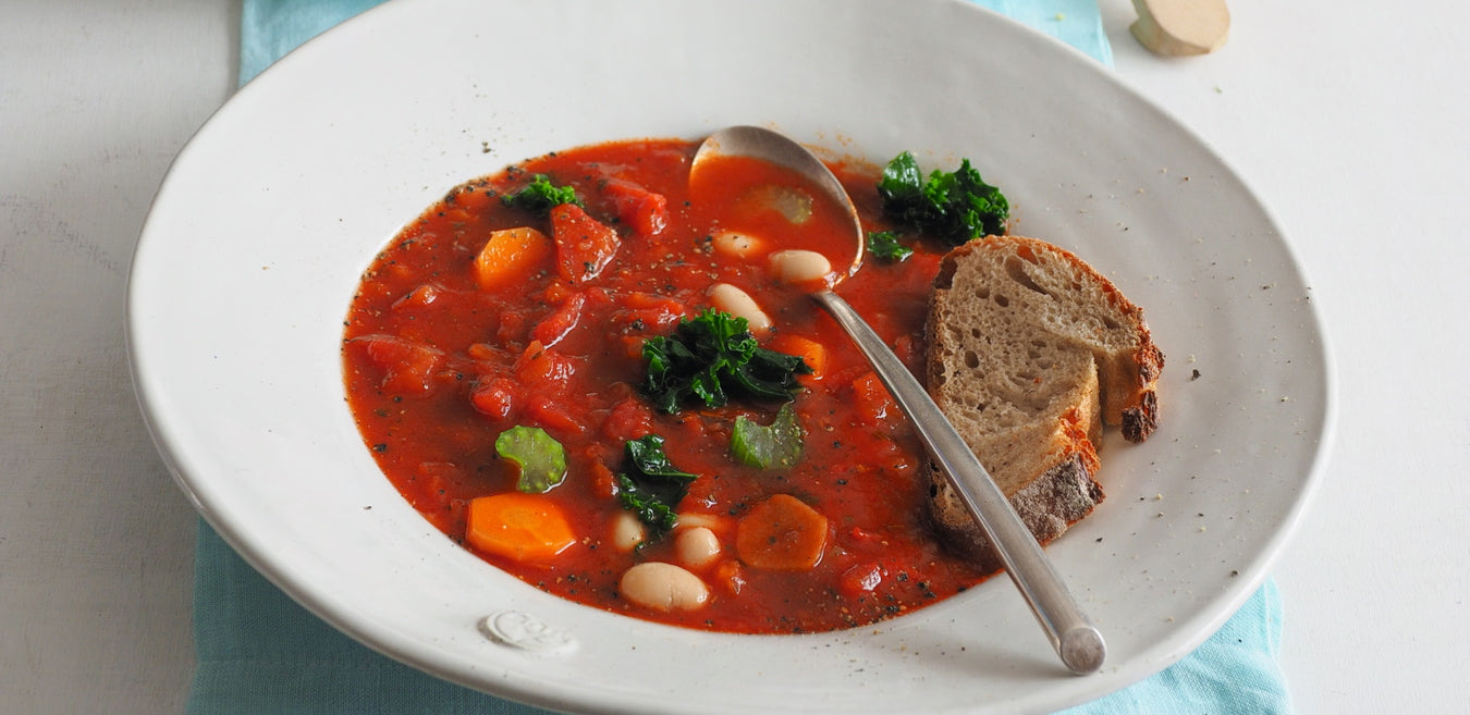 Toskanische Tomatensuppe auf einem weißen Teller mit einem Löffel und einem Stück Baguette