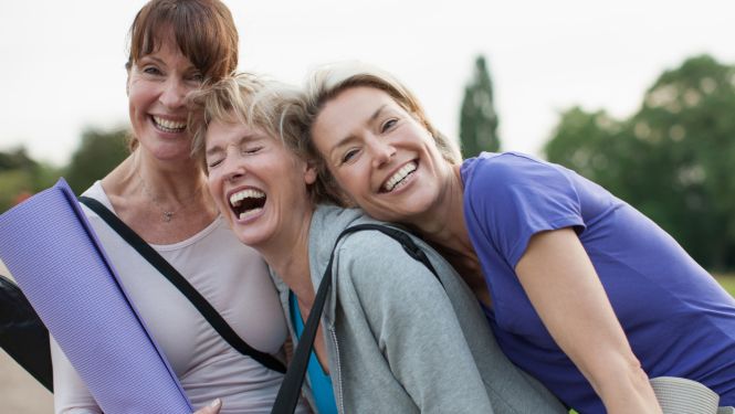 Drei mittelalte Frauen lachen fröhlich mit Yogamatten im Gepäck