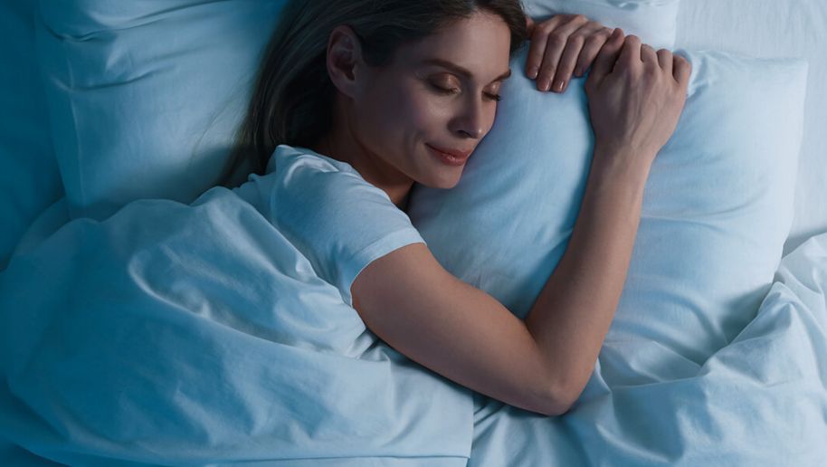 Dunkelhaarige Frau liegt gemütlich schlafend im Bett