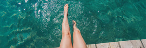 Frauenbeine, die in klaren Wasser vom Steg hängen