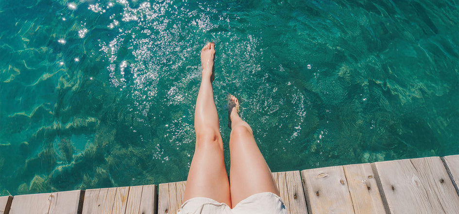Frauenbeine, die in klaren Wasser vom Steg hängen