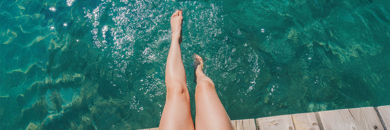 Frauenbeine, die in klaren Wasser vom Steg hängen