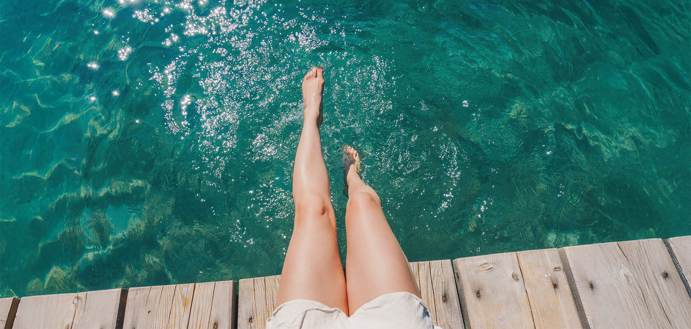 Frauenbeine, die in klaren Wasser vom Steg hängen