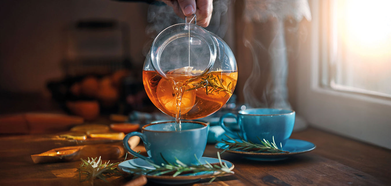 Jemand schenkt aus einer Glasteekanne Tee in eine Tasse