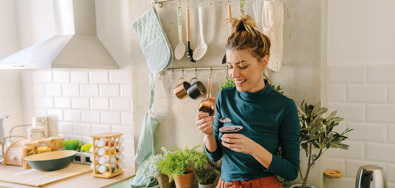 Junge Frau isst Joghurt stehend in der Küche