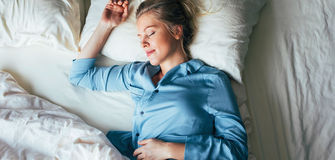 Blonde Frau liegt zufrieden schlafend im Bett mit weißer Bettwäsche