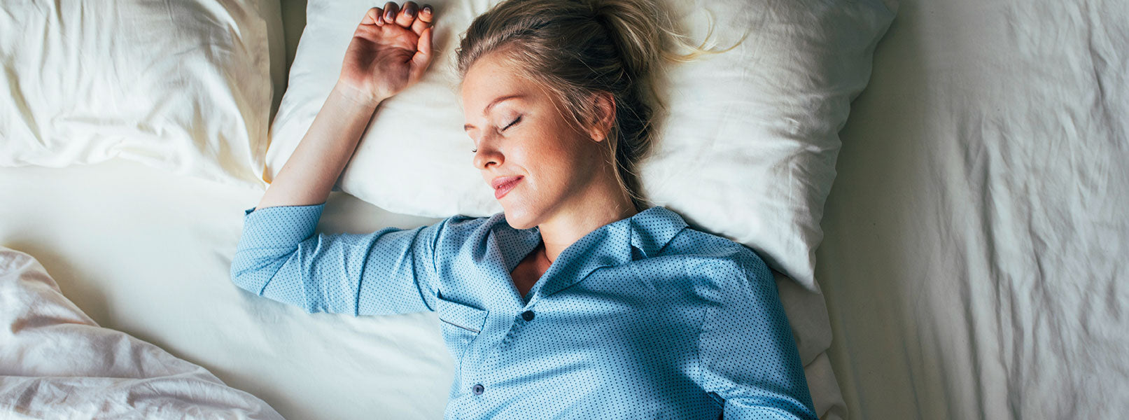 Blonde Frau liegt zufrieden schlafend im Bett mit weißer Bettwäsche