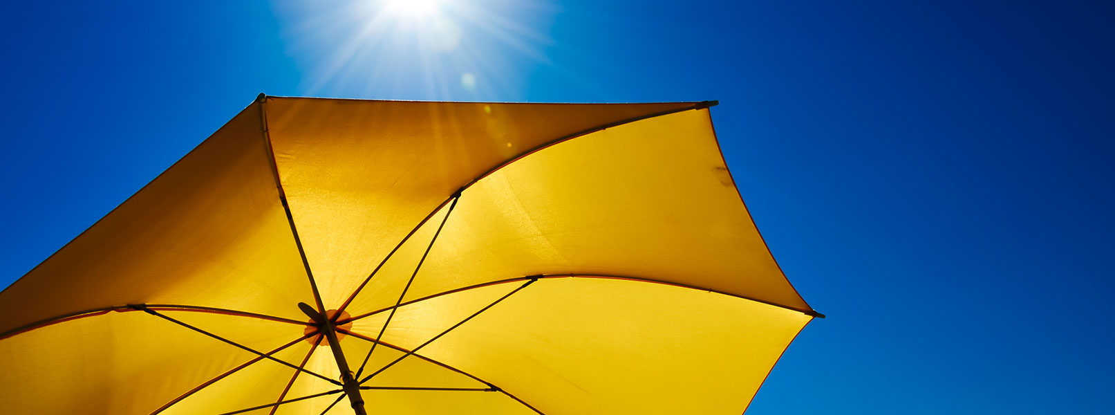 gelber Sonnenschirm vorstrahlend blauem Himmel