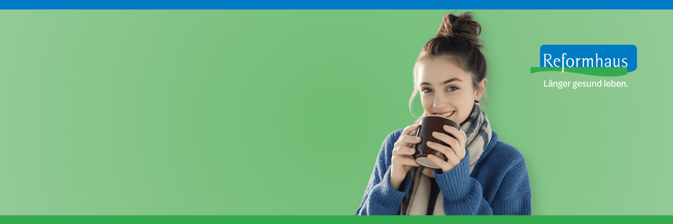 Junge dunkelhaarige Frau mit Teetasse und dicken Schal lächelt freundlich