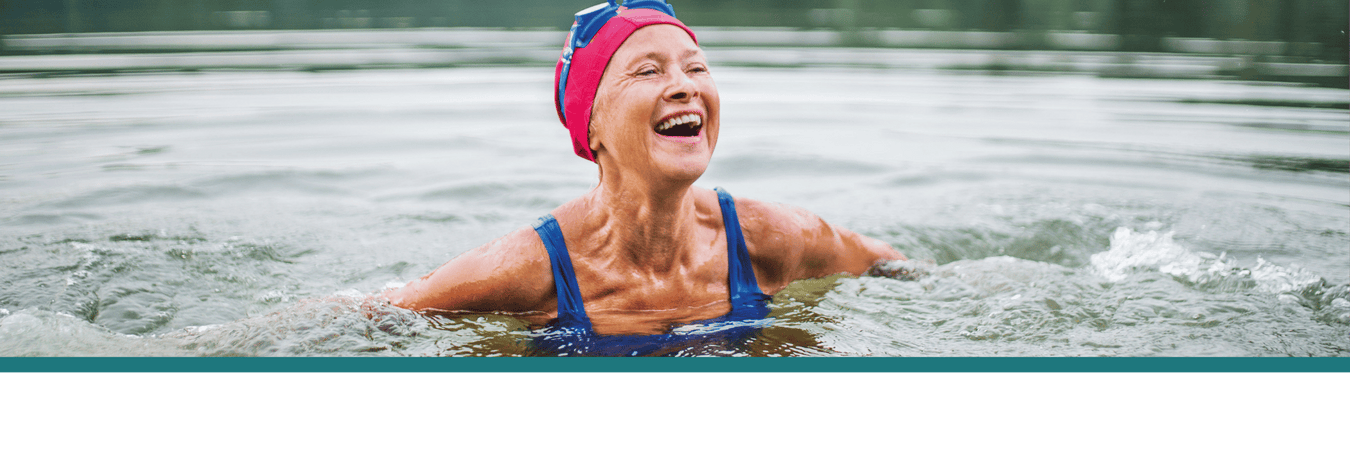 Seniorin mit pinker Badekappe und blauer Schwimmbrille freudig im See