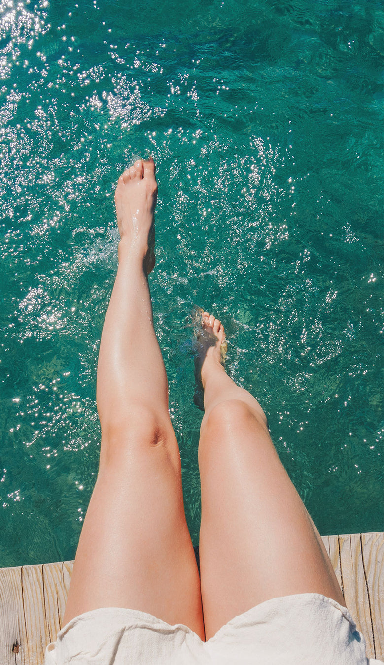 Frauenbeine, die in klaren Wasser vom Steg hängen