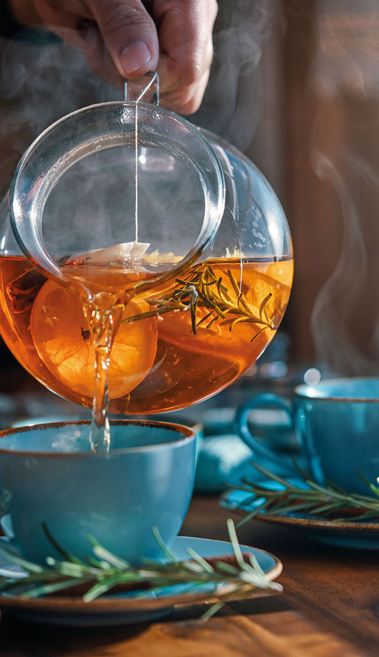 Jemand schenkt aus einer Glasteekanne Tee in eine Tasse