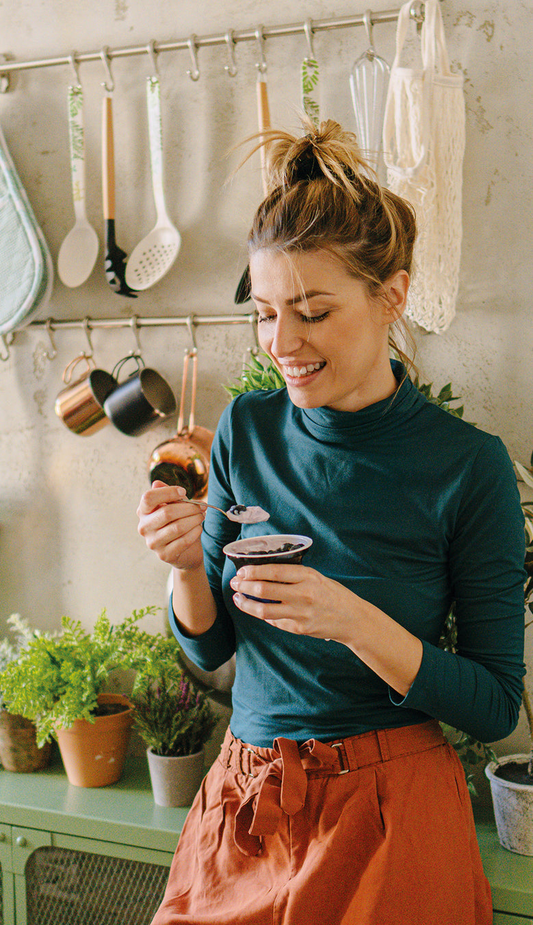 Junge Frau isst Joghurt stehend in der Küche