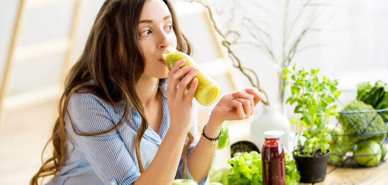 Junge, dunkehaarige Frau trink grünen Smoothie aus Glasflasche