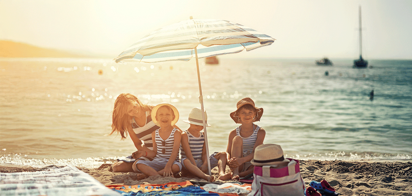 Mutter mit Kindern am Strand unterm Sonnenschirm