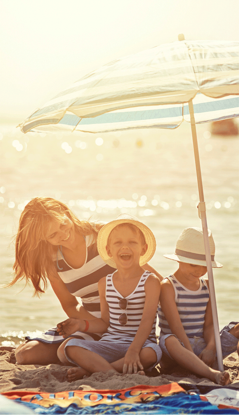 Mutter mit Kindern am Strand unterm Sonnenschirm